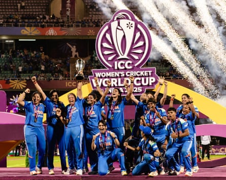 The women’s team in blue kit wearing their medals throw up their hands with fireworks in the background