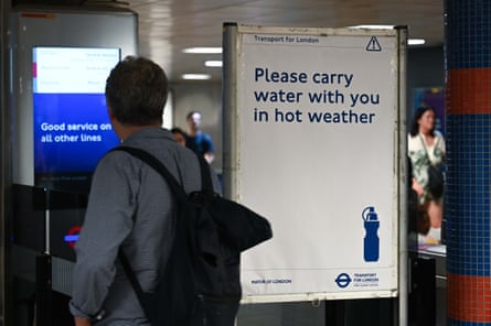 A commuter walks past a London Underground sign urging people to carry water in hot weather