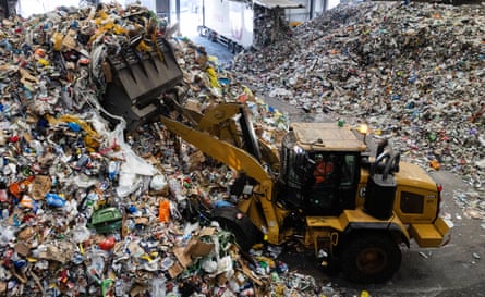 A digger sorts through a mountain of rubbish at a recycling plant