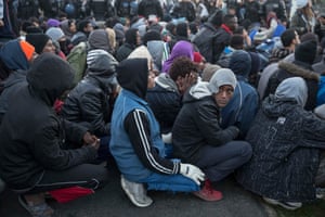 Refugees sit on the ground as they wait for processing