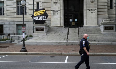 A Washington DC police officer walks past an umbrella reading ‘Defund Police’ on the steps of a city government building, 19 June 2020.