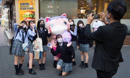 Koronon, a Japanese anti-coronavirus cat mascot poses for a photo with a group of schoolgirls wearing facemasks in Ikebukuro, Tokyo.