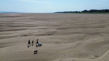 Three people walk on a vast dry river bed