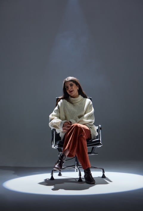 Sirin Kale in a leather chair with a spotlight on her.