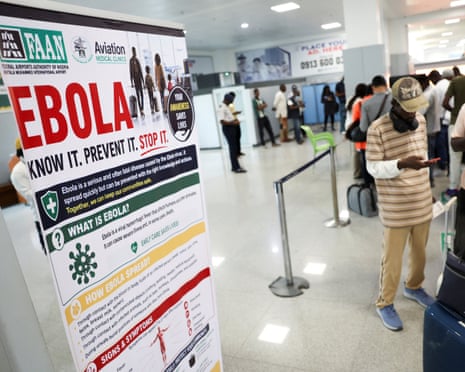 A large Ebola awareness banner stands beside travellers queuing with luggage at Lagos airport