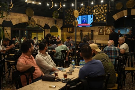 Patrons sitting in a cafe watch a TV broadcast