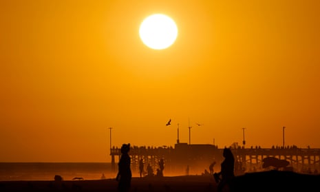 Beachgoers walk along a waterfront as the sun sets