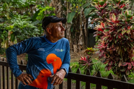 A man in a cap leans on a fence looking out at a tropical garden