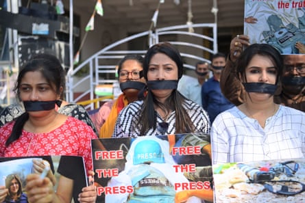 Indian women and men with black bands across their mouths to represent gags hold placards showing photographs of journalists killed in the Gaza war with the words ‘free the press’