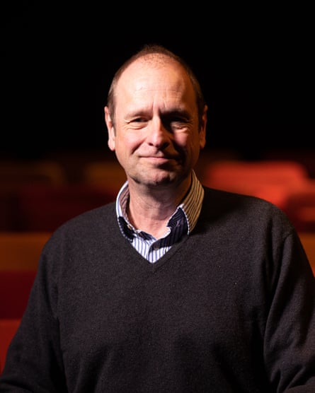He sits in a theatre, posing for the camera