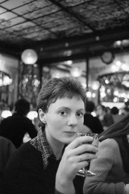 Black and white photograph from 1978 of a short-haired woman sitting in a cafe in Paris, holding a glass of wine