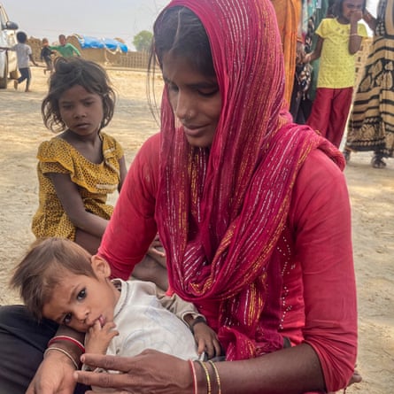 A young Indian woman with a headscarf cradles a very small infant as an older girl looks on