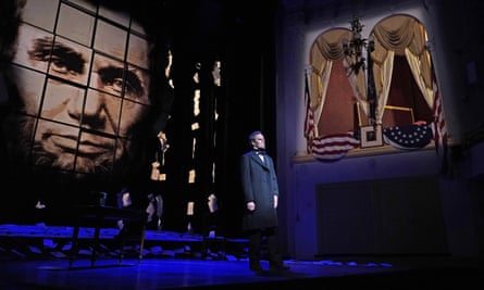 man in suit stands on stage, with an image of Abraham Lincoln projected behind him