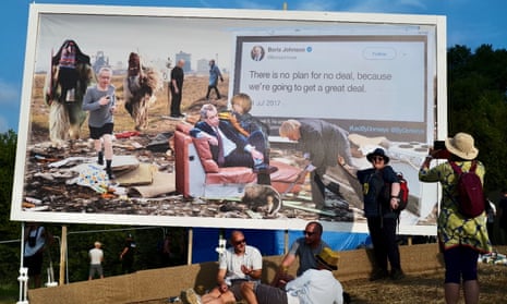 Festival-goers sit under an anti-Brexit billboard, a collaboration by Cold War Steve and Led By Donkeys. 