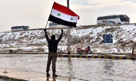 A man waves a Syrian national flag to a convoy carrying the last rebel fighters out of Aleppo.