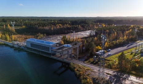 An aerial view shows a dam on the Oulu River, Finland, surrounded by forest and power lines.