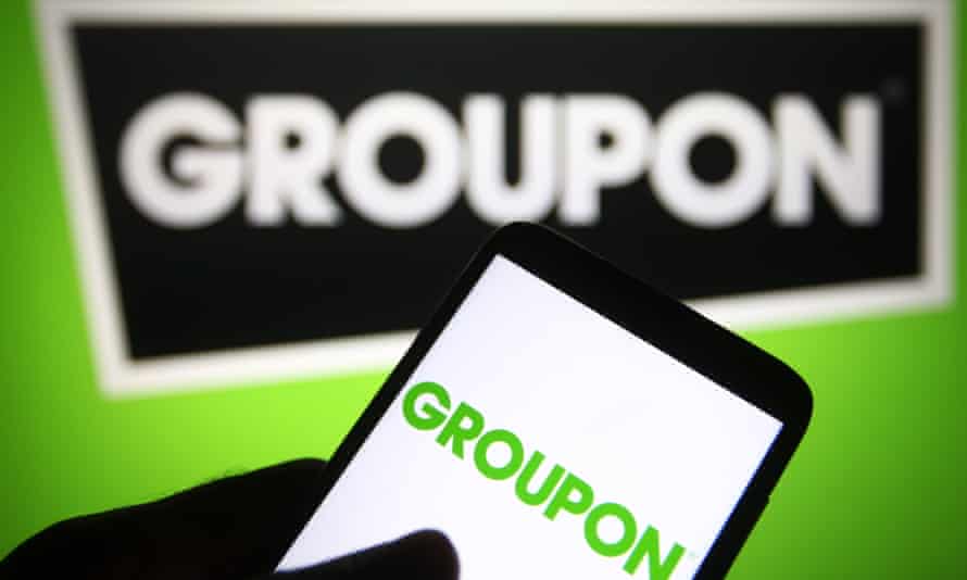 A Groupon logo is seen on a smartphone and a PC screen.