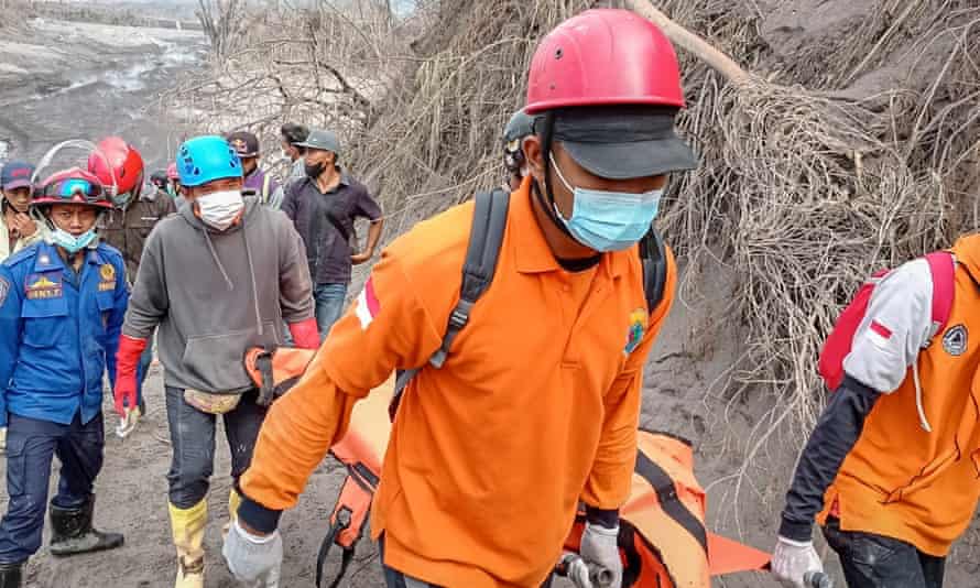 Rescuers carrying the body of a victim at an area affected by the eruption of Mount Semeru