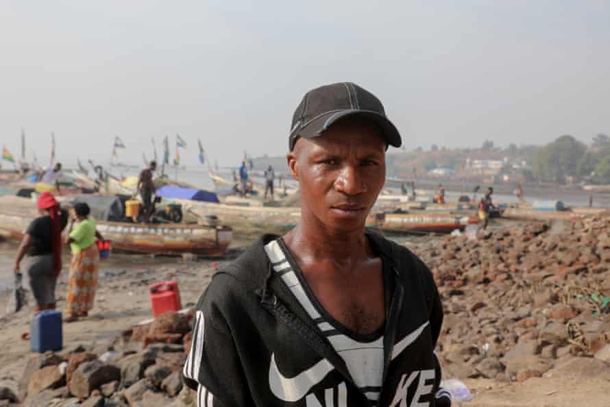 A Fisherman standing on the beach with boats behind him