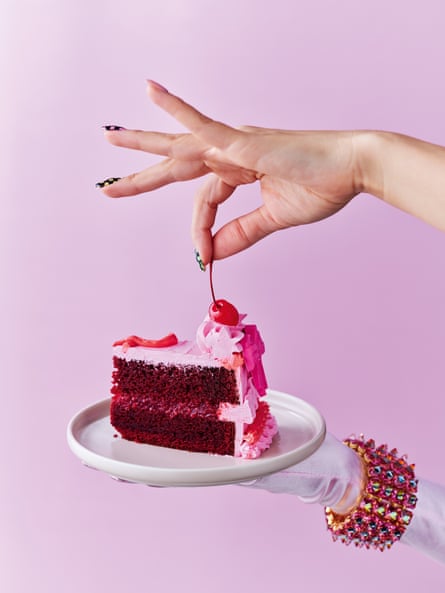 Slice of red velvet cake with pink buttercream and raspberry compote filling with cherries on top, on a pink background