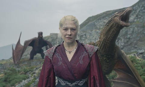 film still with woman in fantastical clothes standing with two dragons behind her