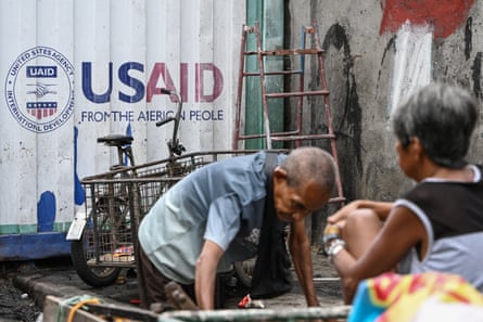 Une pancarte pour USAid est visible sur un conteneur de fret derrière des personnes triant des objets récupérables pour les vendre à des brocantes à Manille, aux Philippines, lundi.
