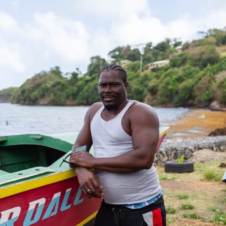 A young man poses in a cove with his arm on a fishing boat