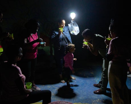 People eat from plastic cups as a woman holds a lamp over a child