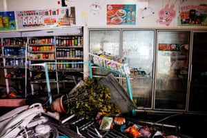 A moped and a jumble of shop items and shelves lie on the ground with shelves and fridges stacked with soft drinks