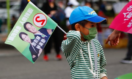 A child in a face mask and sunhat holding an election flag with the faces of DPP candidates