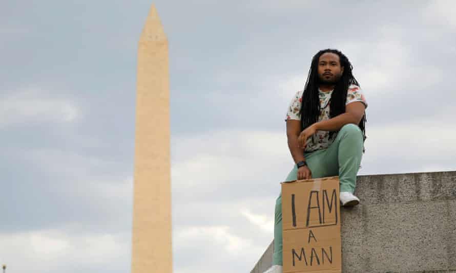 Aaron Xavier Wilson holds the same banner he displayed during a ‘Get Your Knee Off Our Necks’ march in support of racial justice last year as he poses for a photo on the National Mall in Washington in May 2021.