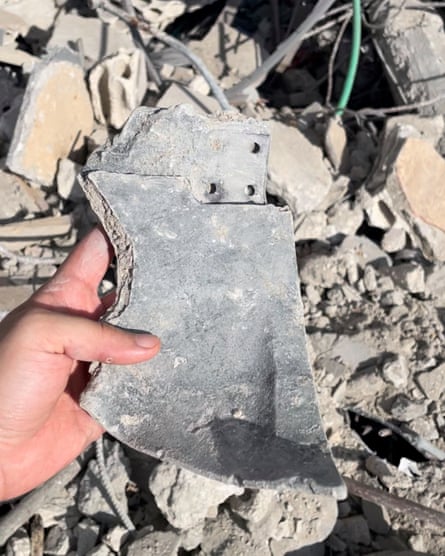 A hand holding a metal fragment over a pile of rubble and wires