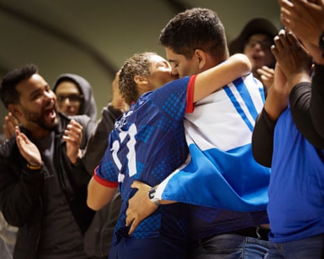 A woman in a dark blue football top and man draped in a blue and white flag kiss surrounded by cheering football fans
