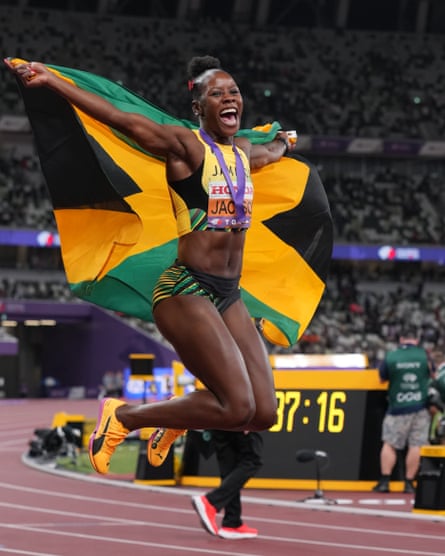 A delighted black athlete jumps on a track holding the Jamaican flag
