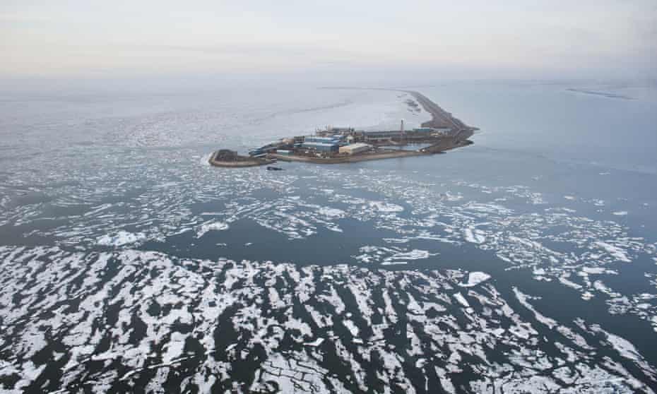 An oil well drilling platform on a man-made island and surrounded by broken sea ice.