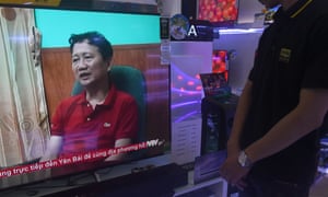 A store employee (R) watches a screen showing Trinh Xuan Thanh speaking in a clip aired by Vietnam’s state television VTV, in Hanoi