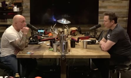 Joe Rogan and Elon Musk sitting facing each other across a table with microphones