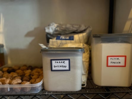 A pantry shelf containing a tray of nuts, and clear plastic containers containing sugar and flour.