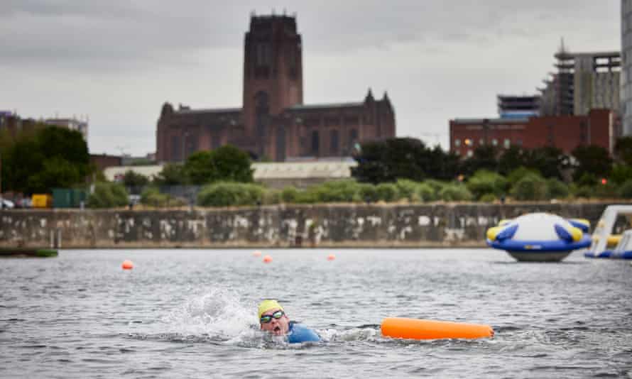 A person in a yellow swimming hat and goggles swimming with an orange float