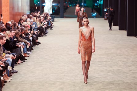 Models in dresses on a runway as people watch from the side