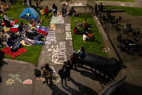 Nighttime view of tents, students and walkways covered with pro-Palestine chalk signs.