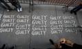 At least six rows of four words in white and all-caps saying GUILTY on dark grey pavement.