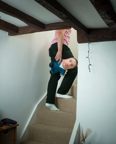 Comedian John Robins climbing a staircase, caput retired of shot, holding his Taskmaster doll, March 2026