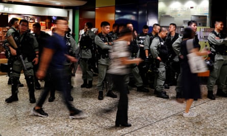 Riot police wait at a Mass Transit Railway (MTR) station as commuters walk past in Hong Kong