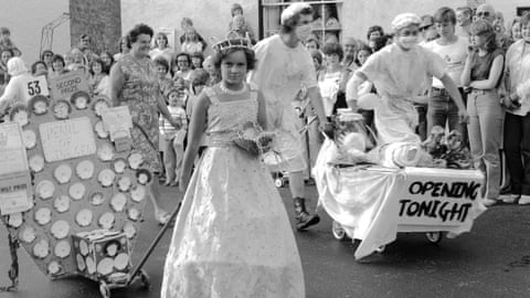 A girl in a gown and crown tows a 'pearl of the sea' float with a 'second prize' card attached