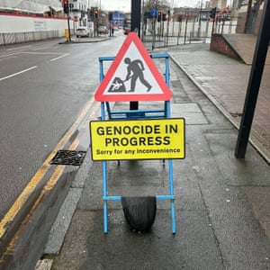 A roadworks sign with an image featuring a stick man burying a child, and the words 'GENOCIDE IN PROGRESS. Sorry for any inconvenience'