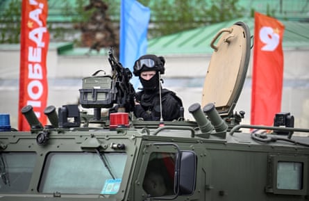 A soldier in all-black uniform sits at a gun turret atop of green armoured vehicle