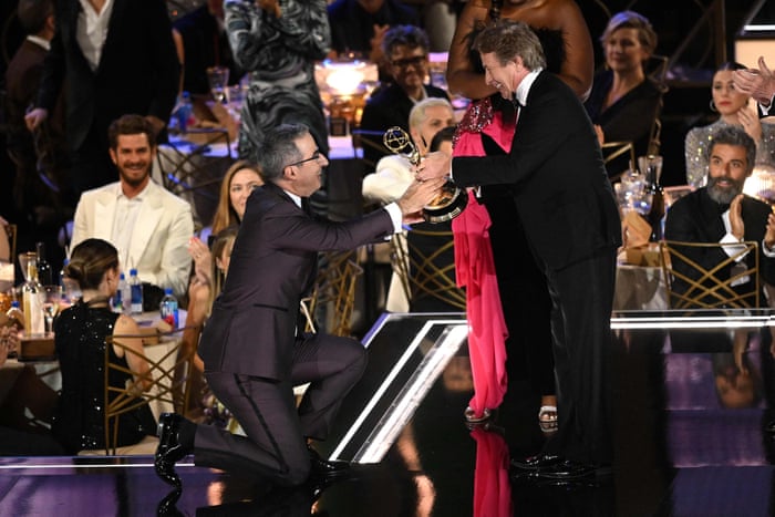 John Oliver kneels as he accepts the award for best variety talk series.