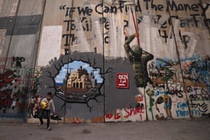 A child plays with a yellow ball in front of graffiti on a wall