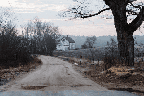 A white barn seen in the distance past a dirt road.